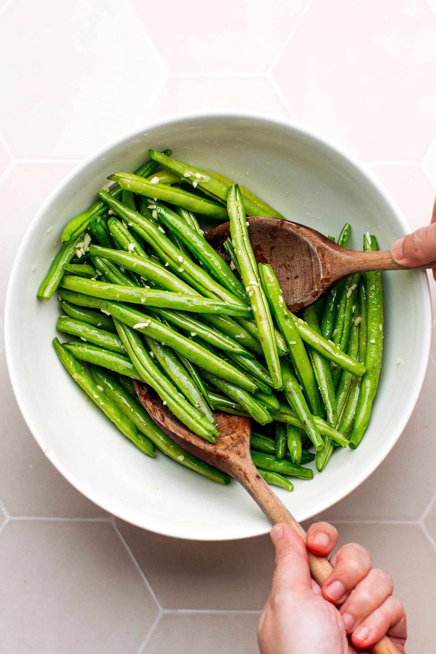 Tossing green beans with garlic, salt, and pepper.