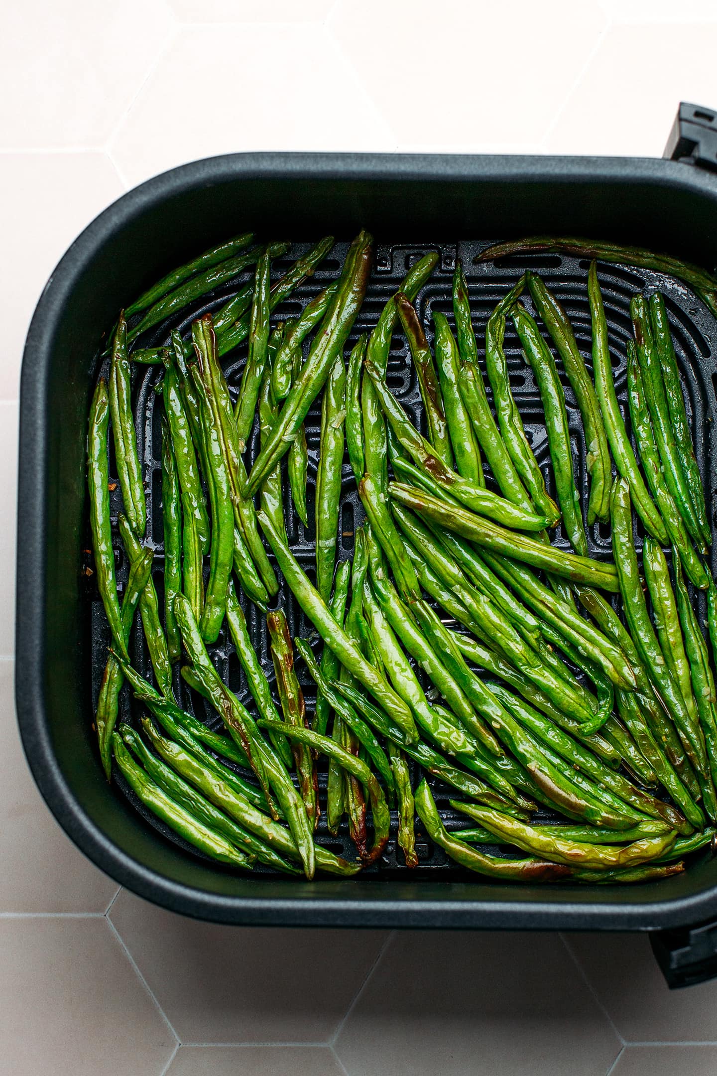 Cooked green beans in an air fryer basket.