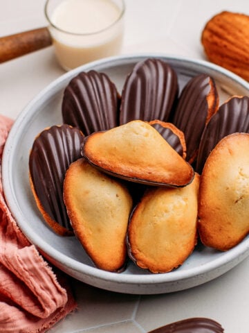 Vegan madeleines dipped in dark chocolate on a plate.