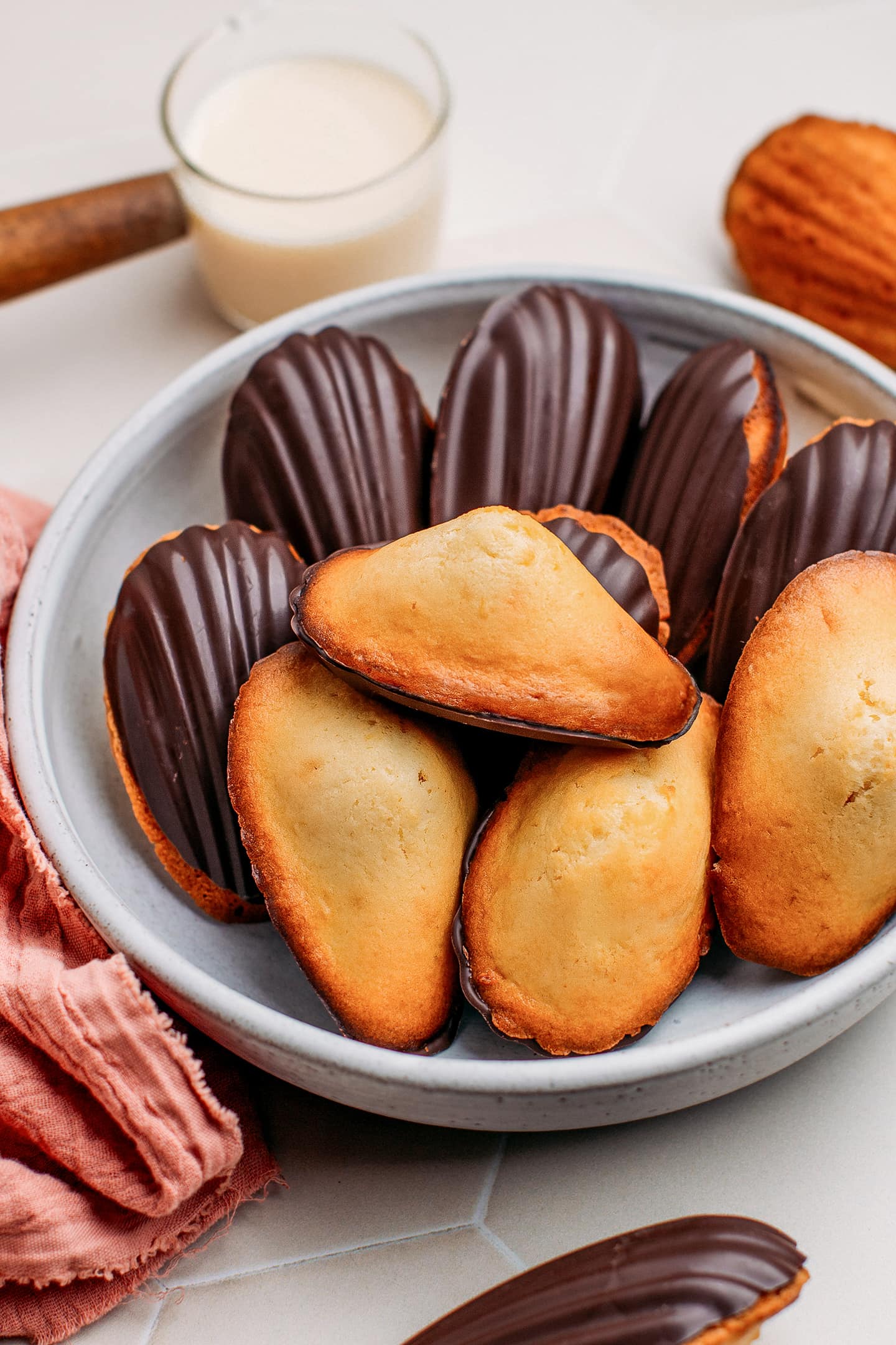 Vegan madeleines dipped in dark chocolate on a plate.