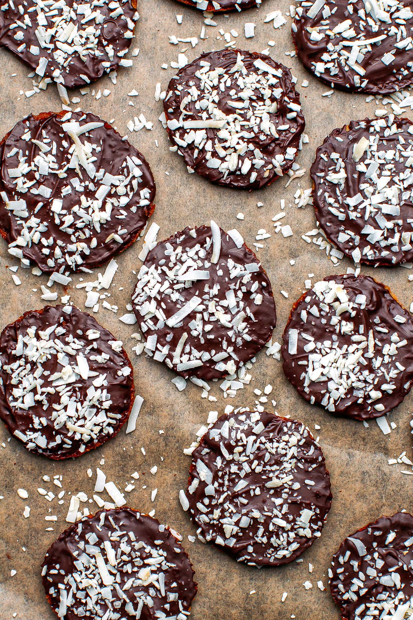 Thin cookies coated with dark chocolate and shredded coconut on a baking sheet.