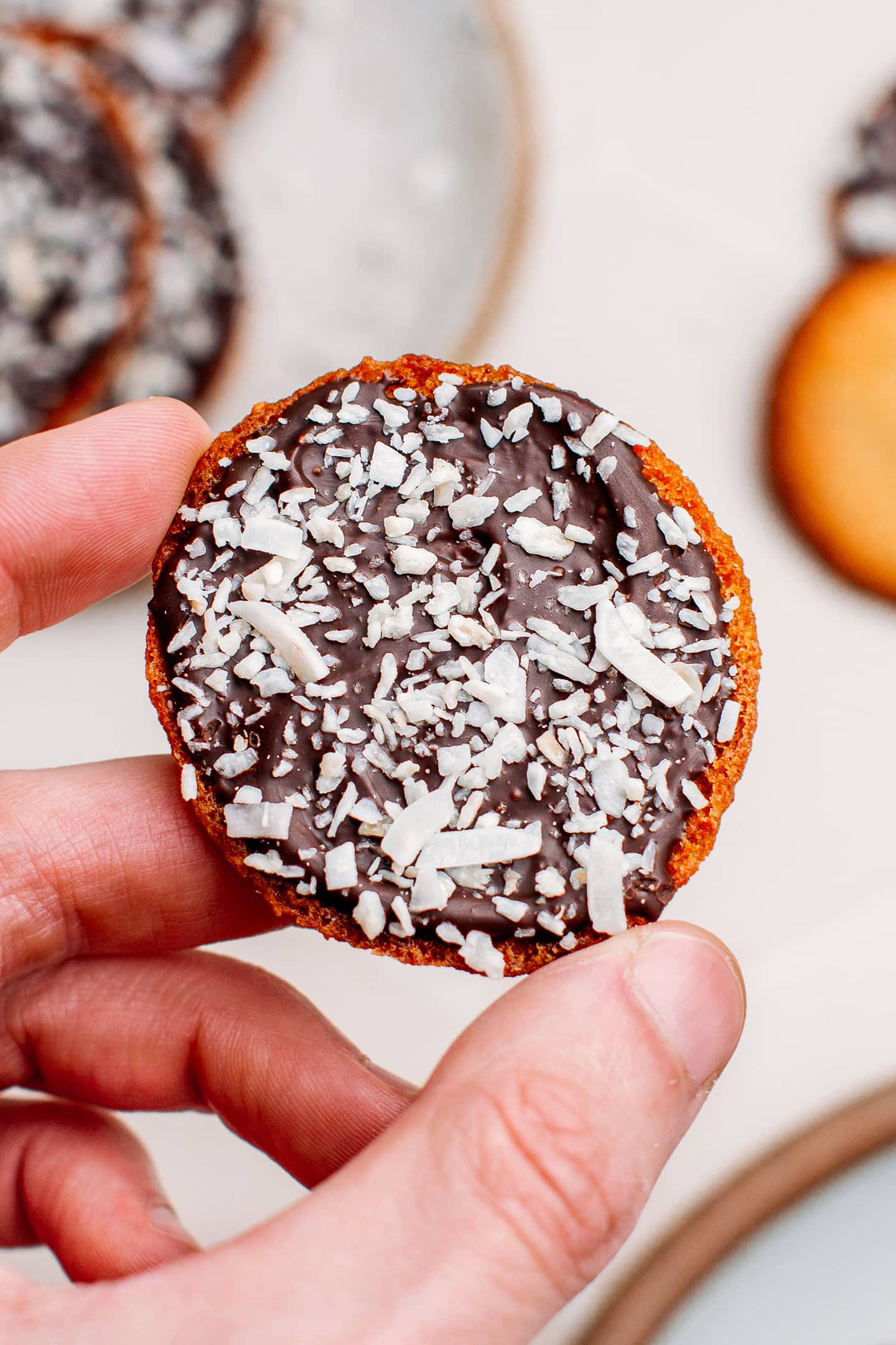 Holding a thin cookie composed of dark chocolate and coconut.