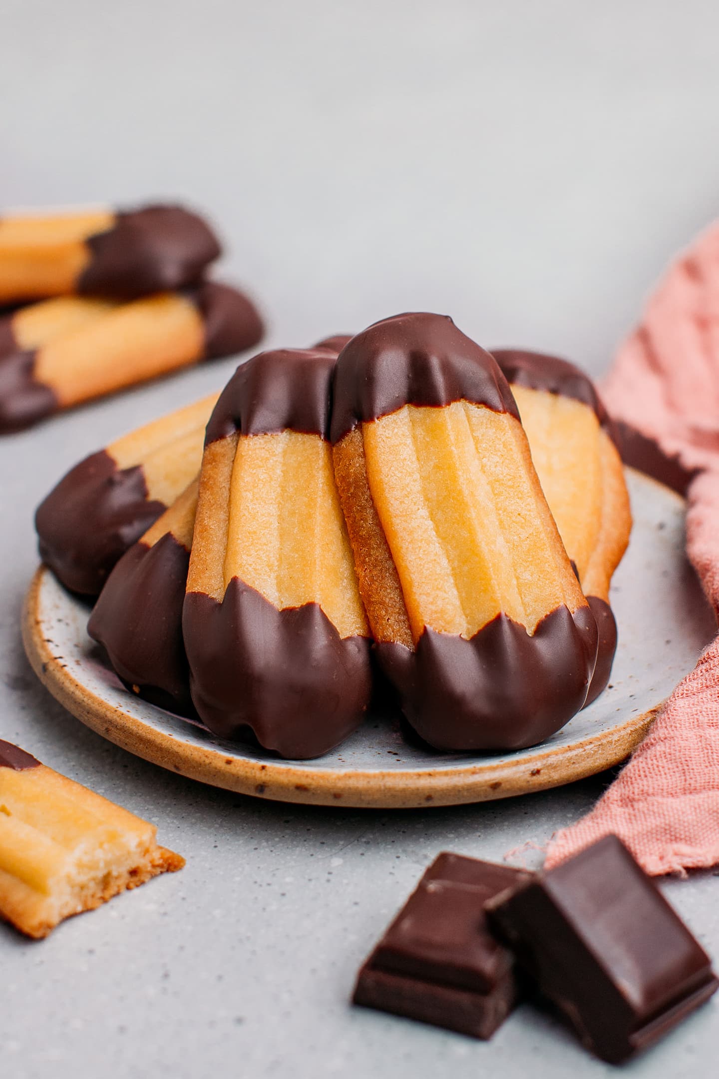 Vegan spritz cookies dipped in dark chocolate on a small plate.