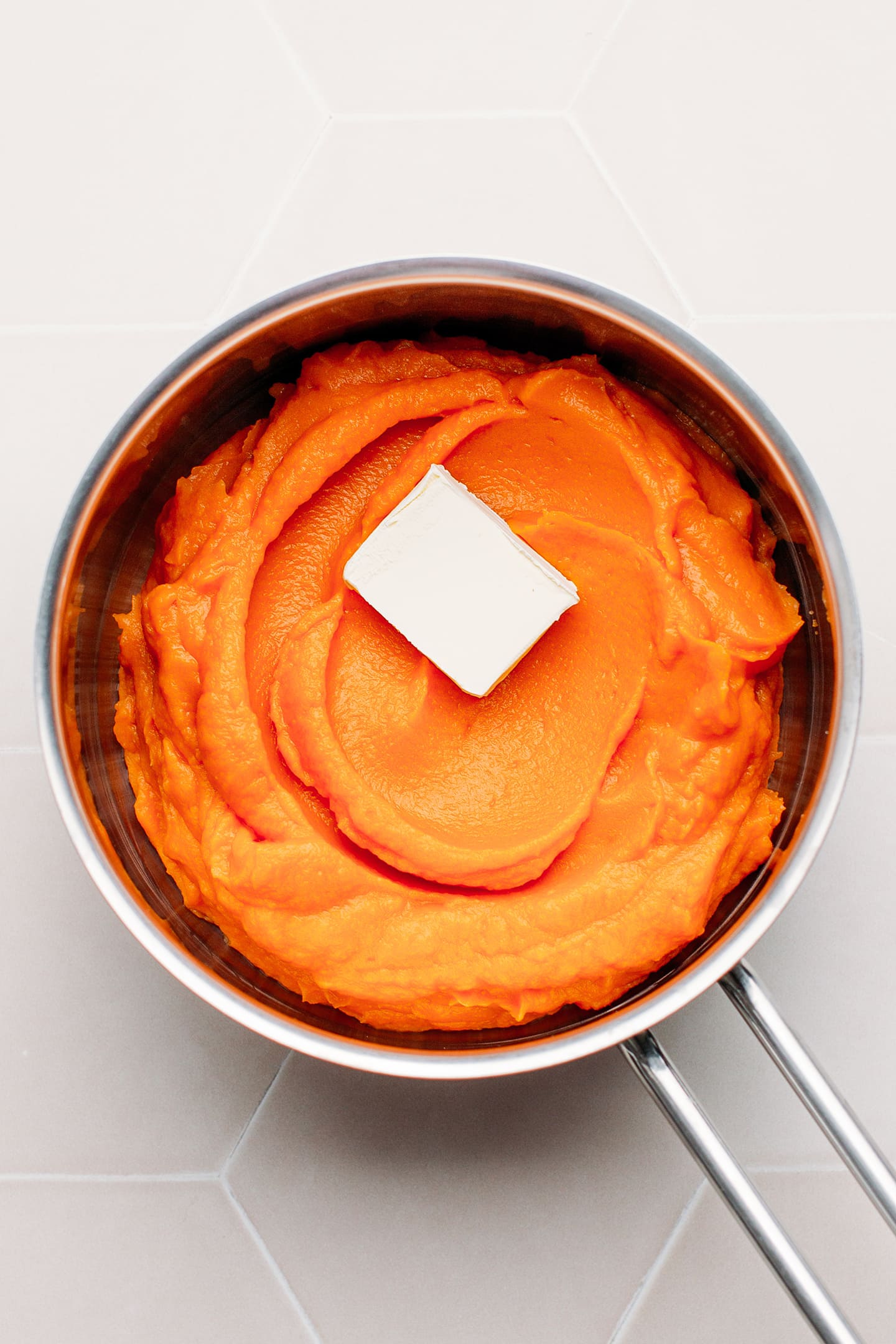 Mashed sweet potatoes and butter in a saucepan.