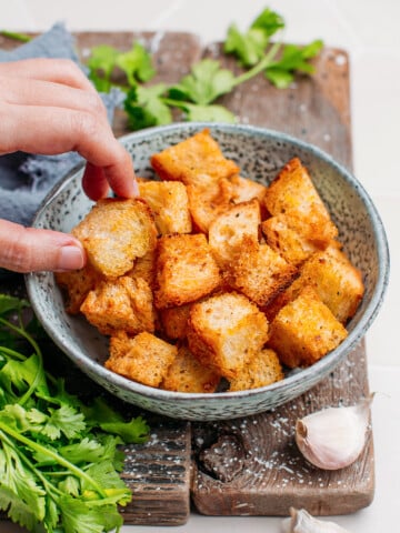 Hand holding a piece of crouton over a serving bowl.