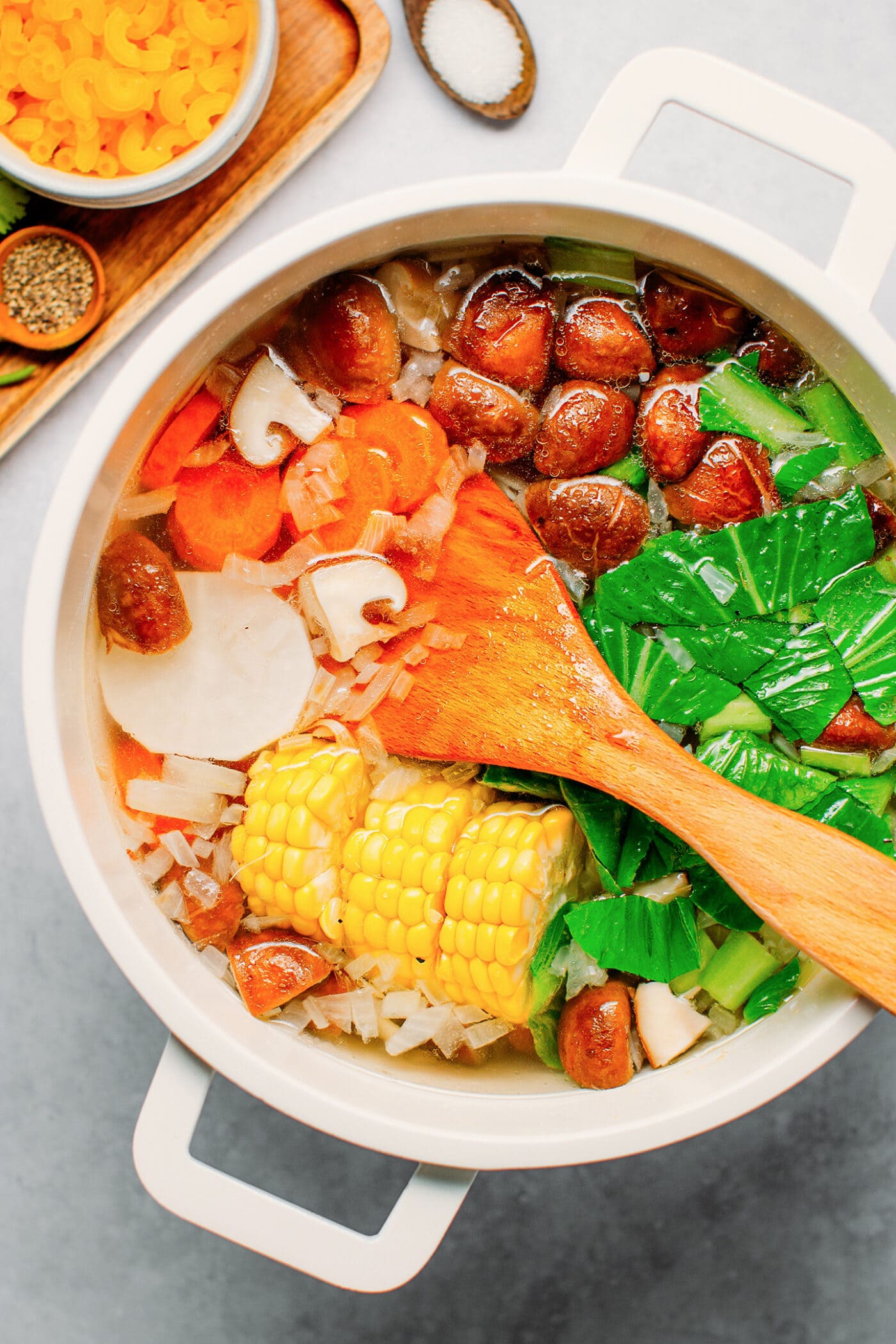 Vegetable broth in a pot with corn, carrot, radish, and mushrooms.