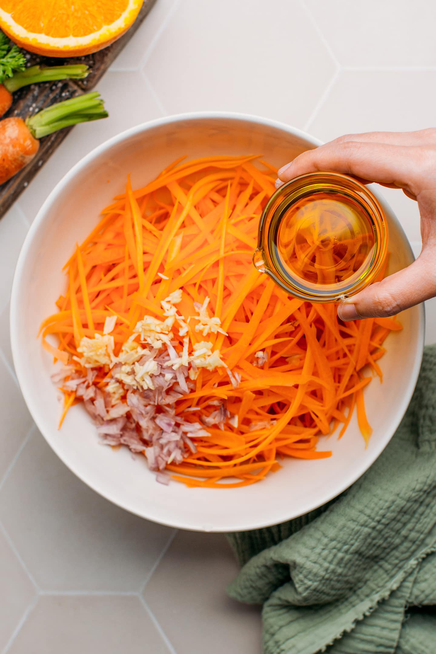 Pouring olive oil into a bowl containing grated carrots.