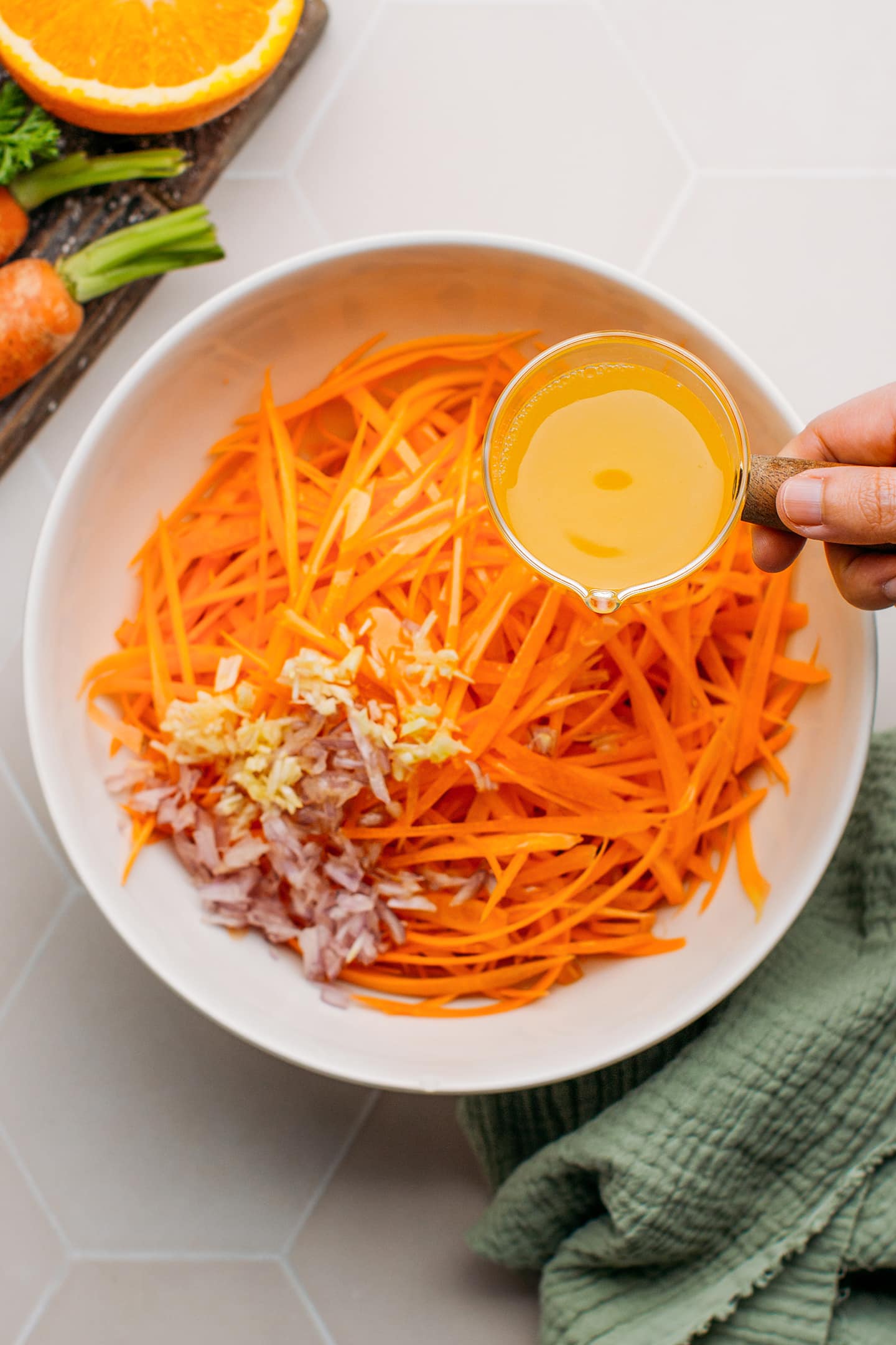 Pouring orange juice into a bowl containing grated carrots.