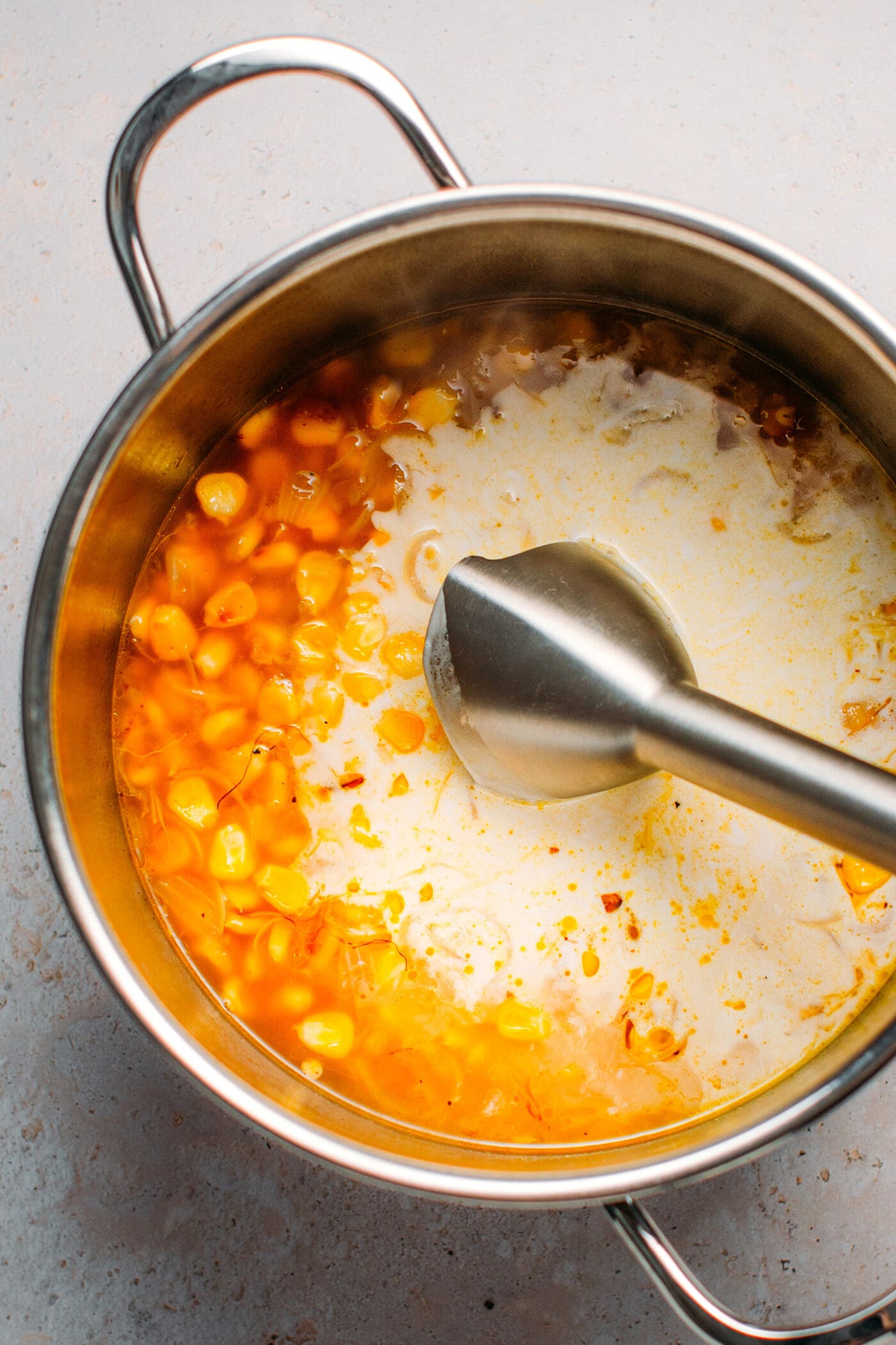 Immersion blender in a pot with corn, water, and coconut cream.