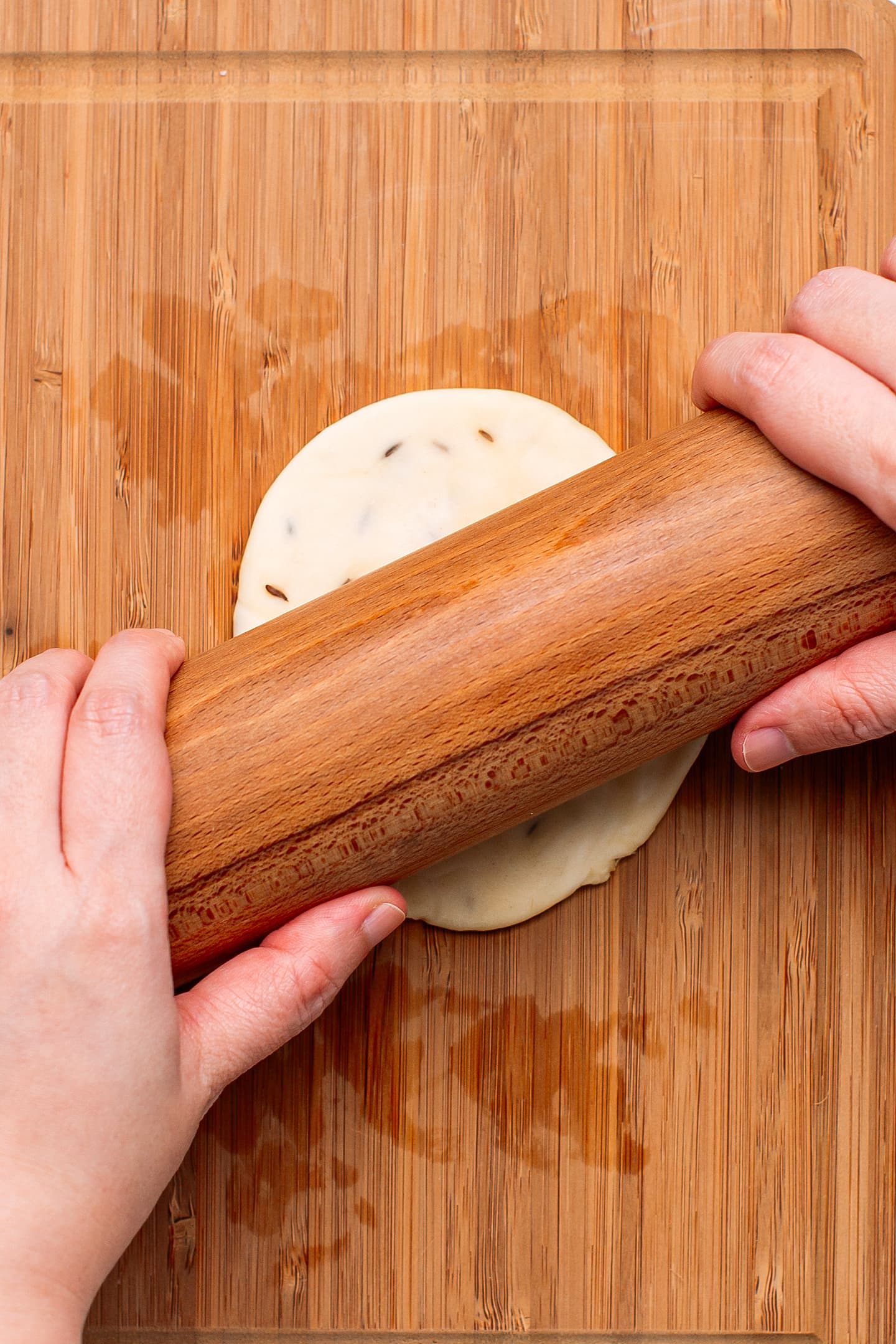 Flattening samosa wrapper on a wooden board.