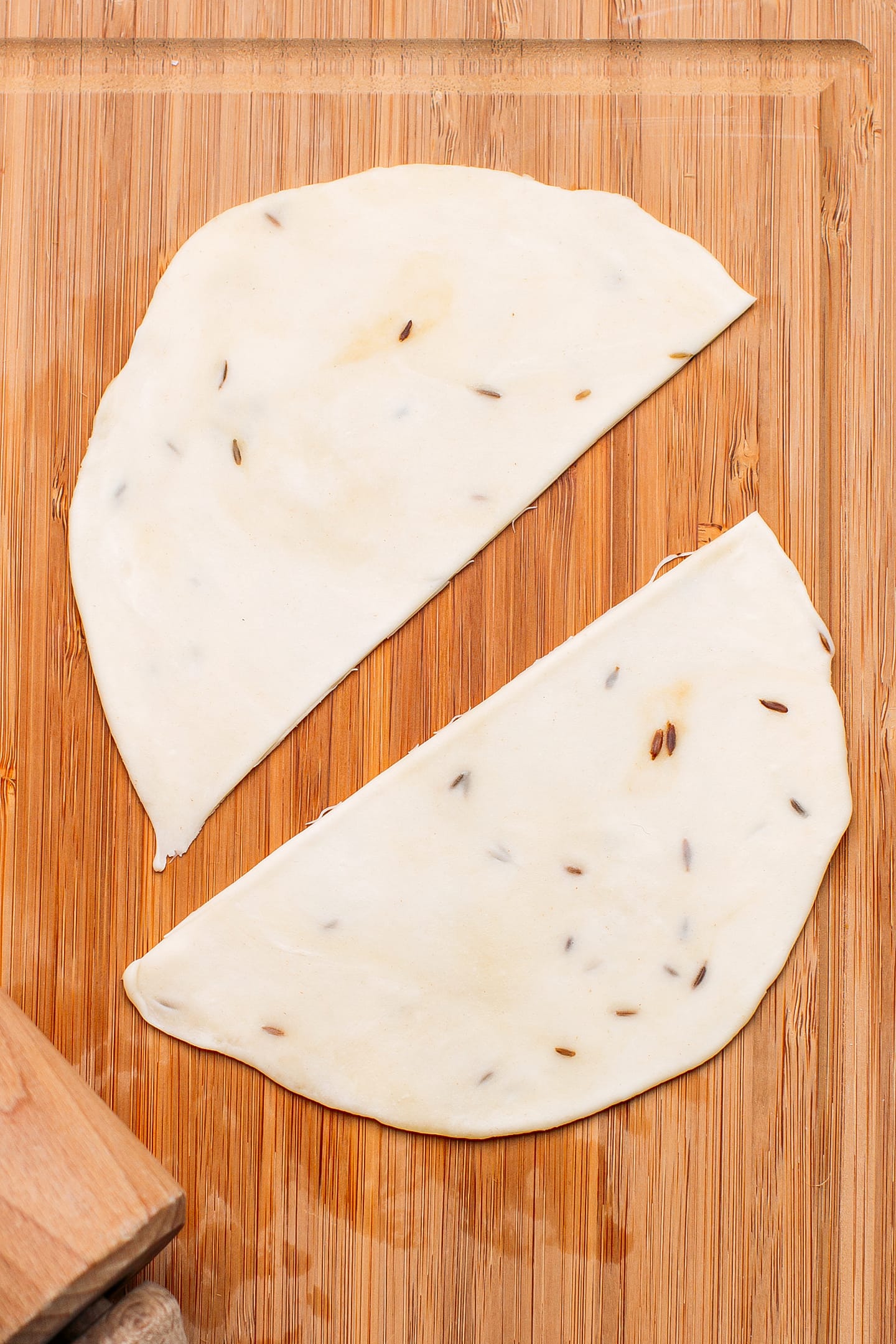 Halved samosa wrapper on a wooden board.