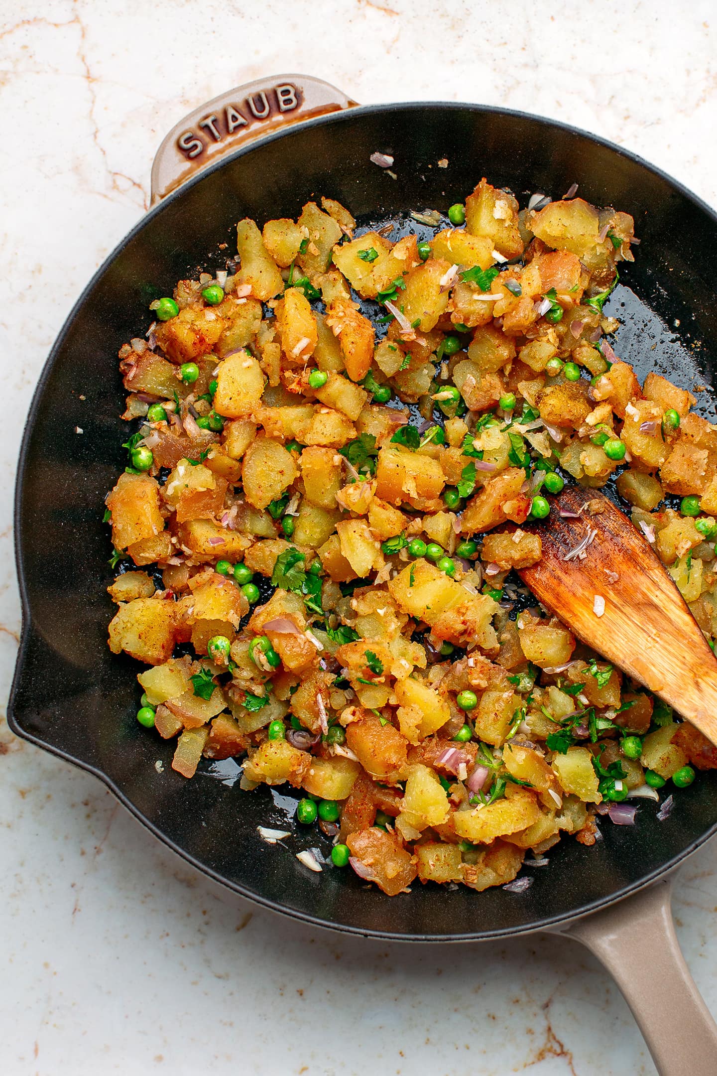 Sautéed potatoes with green peas and cilantro in a skillet.