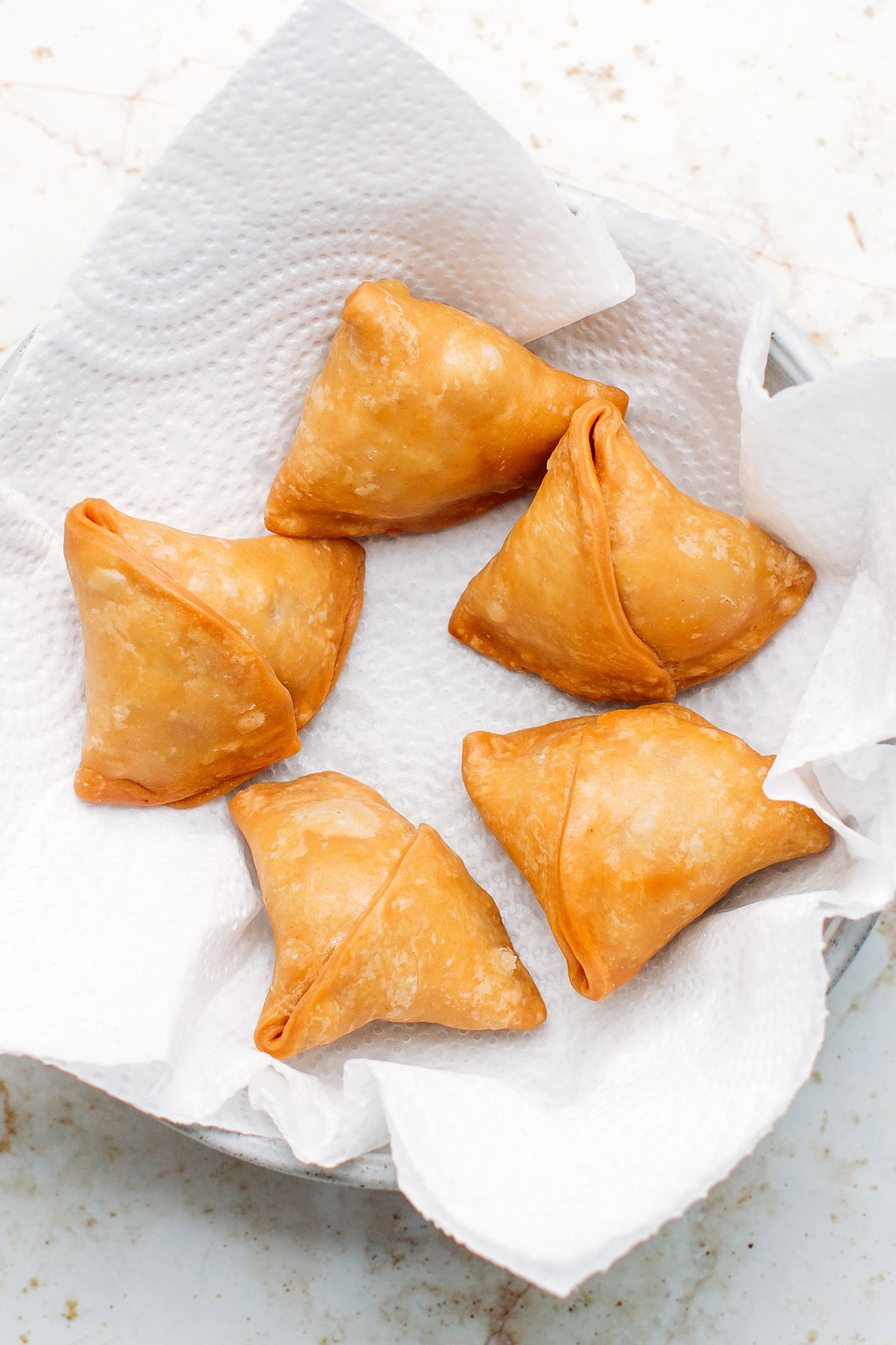 Deep-fried samosas on a plate lined with kitchen paper towel.