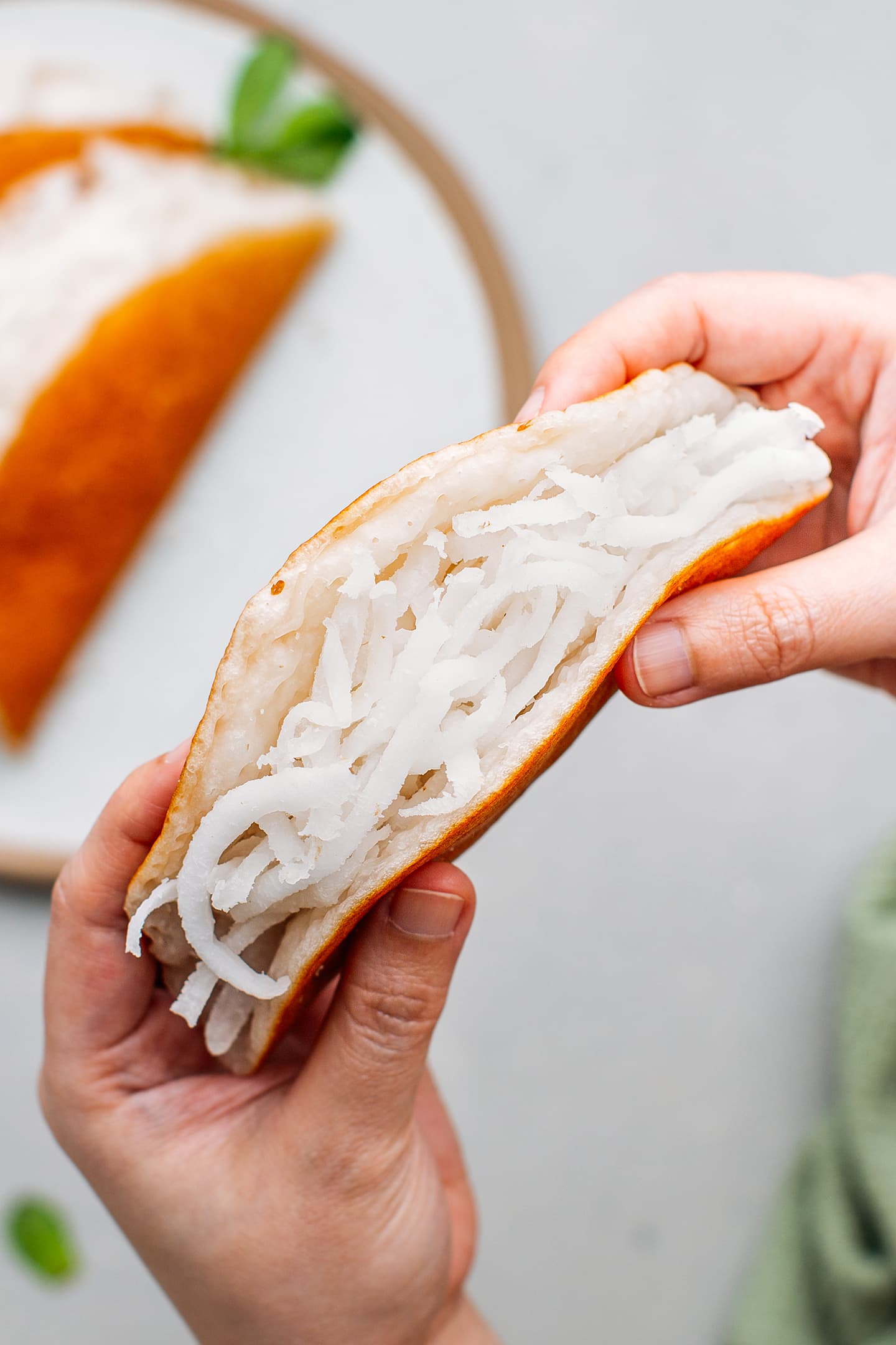 Holding a pancake filled with grated coconut.