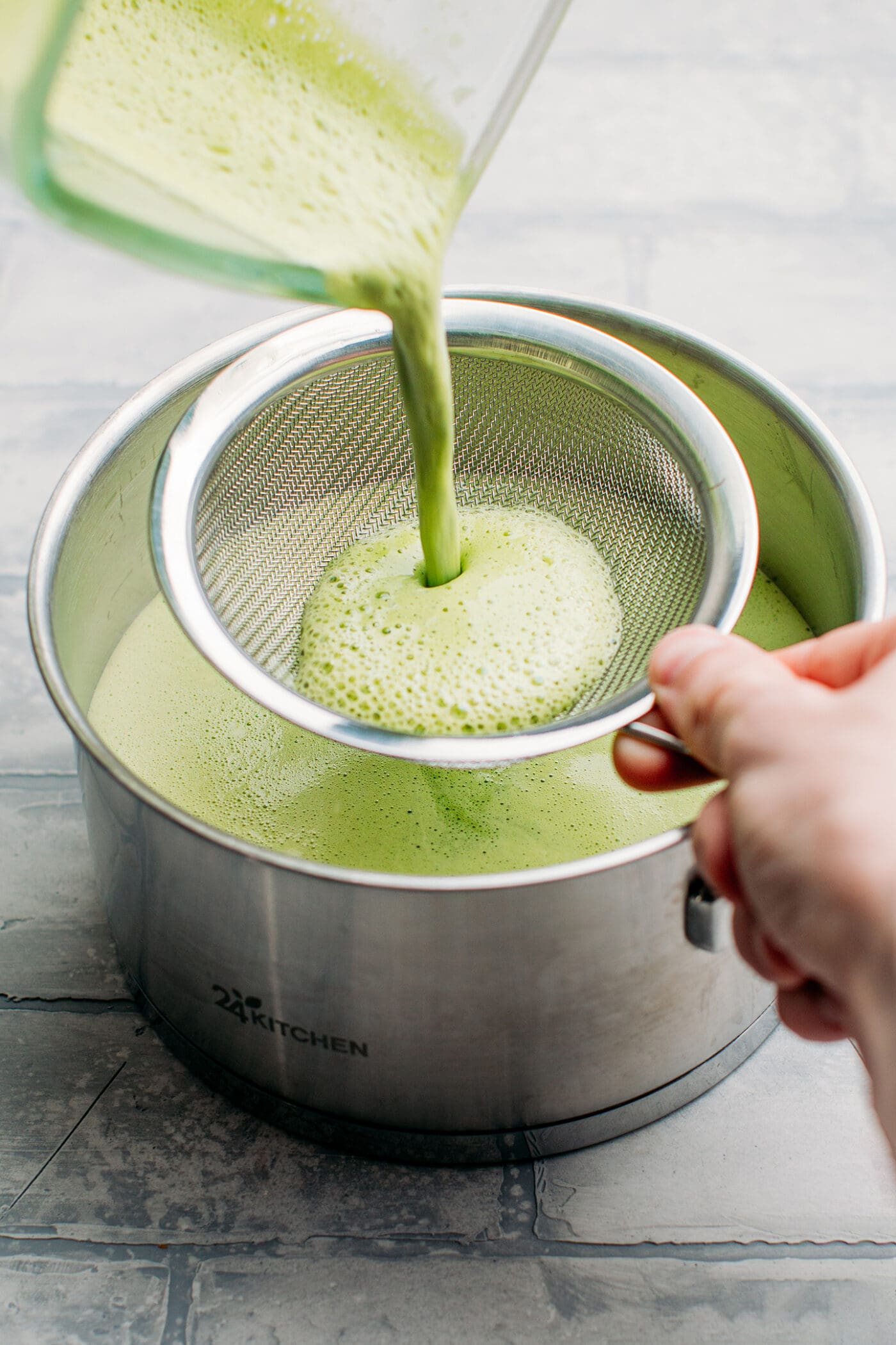 Straining matcha milk through a fine-sieve mesh.