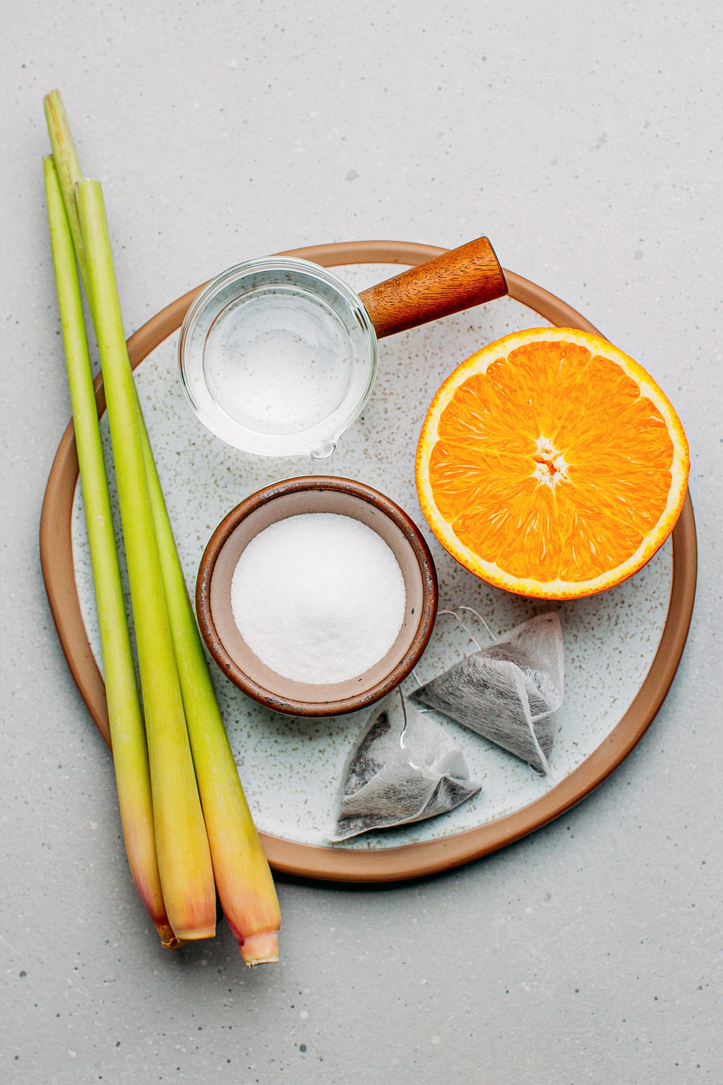 Ingredients like lemongrass stalks, orange, tea bags, and sugar.