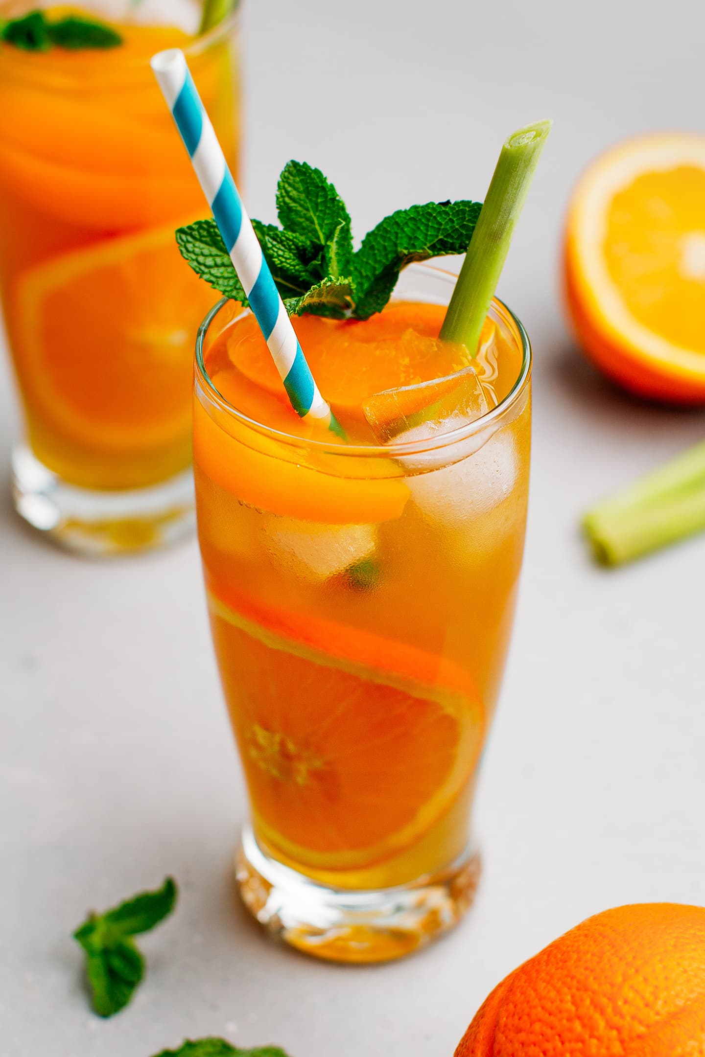 Glass of iced tea with orange slices, lemongrass, and mint leaves.