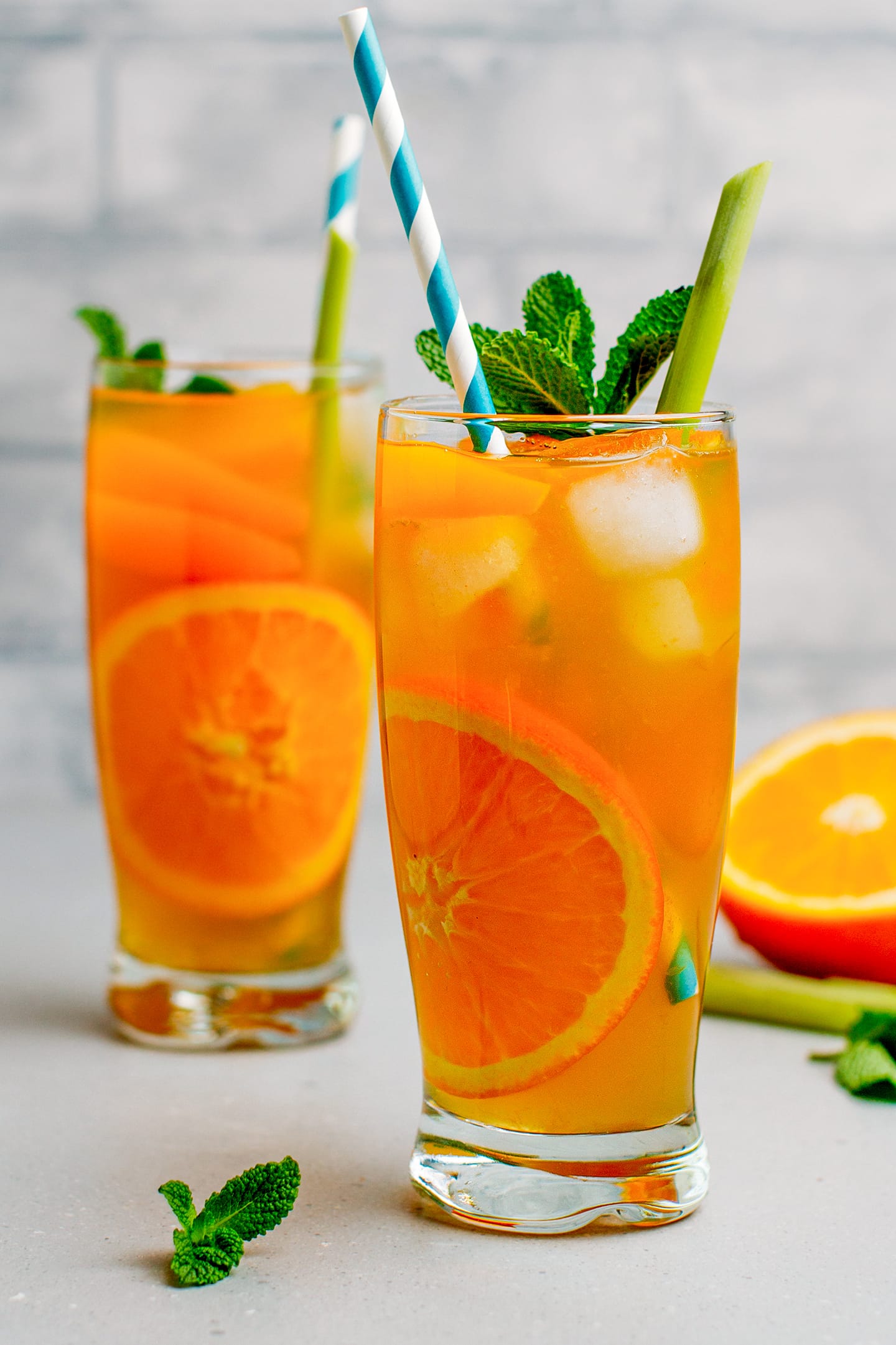 Two glasses of iced tea with orange slices, lemongrass, and mint leaves.