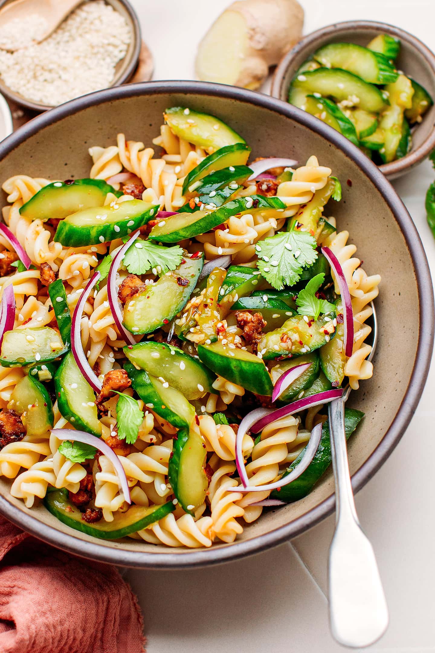 Close-up of pasta salad with smashed cucumbers, red onions, and sesame seeds.