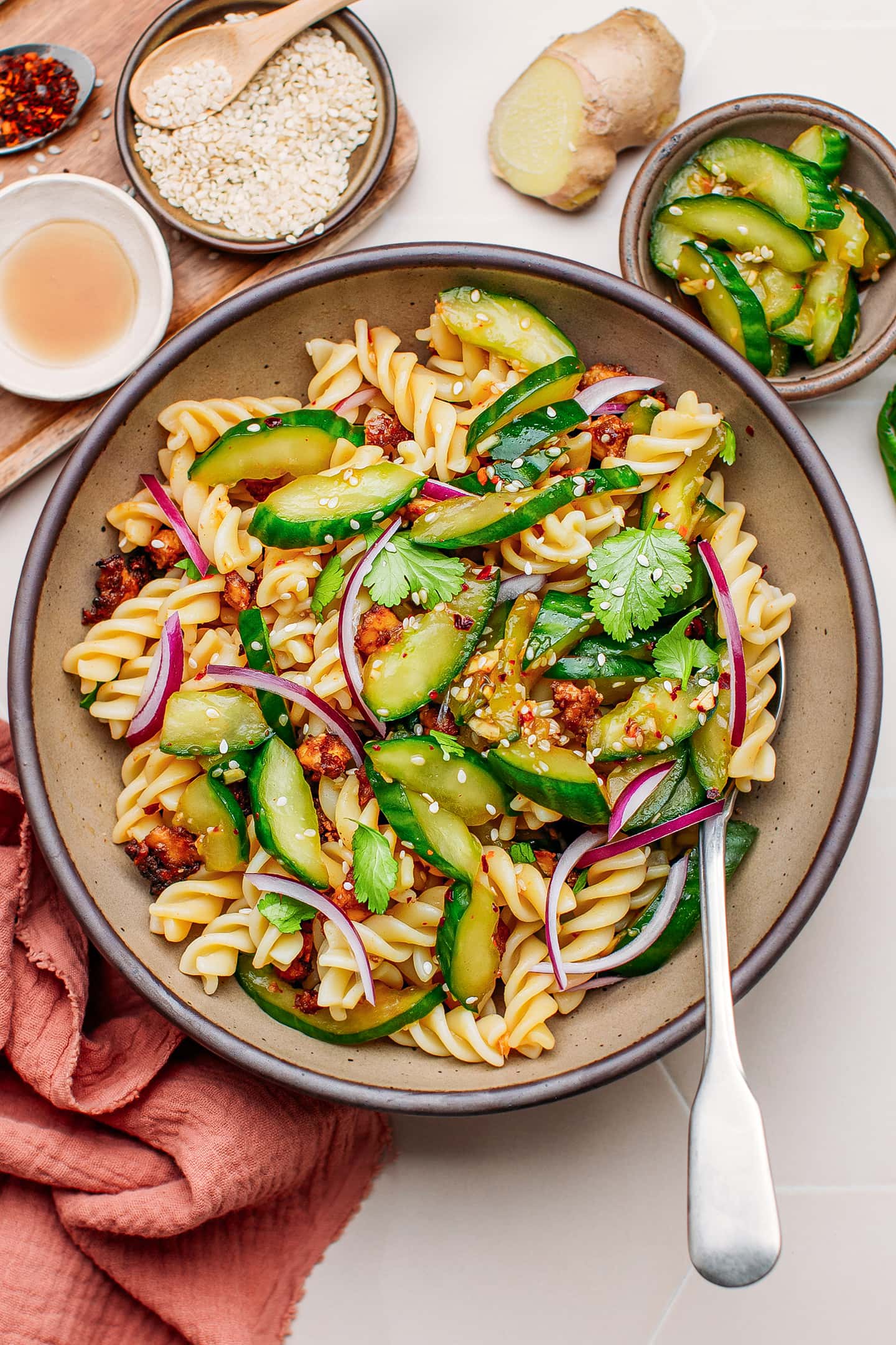 Smashed cucumbers, pasta, and red onions in a bowl.