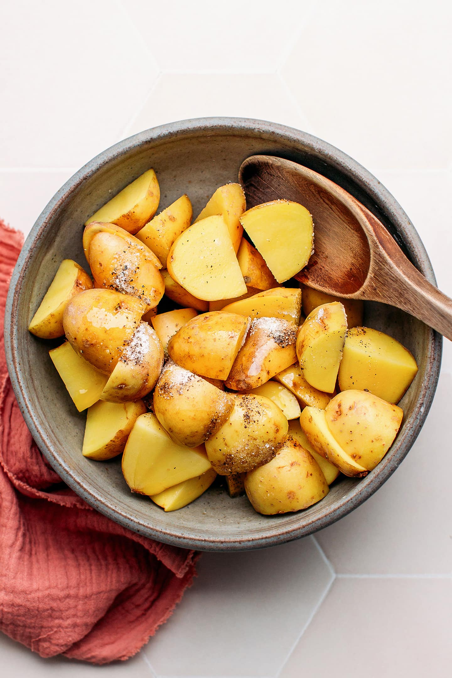 Quartered potatoes tossed with salt and pepper in a bowl.