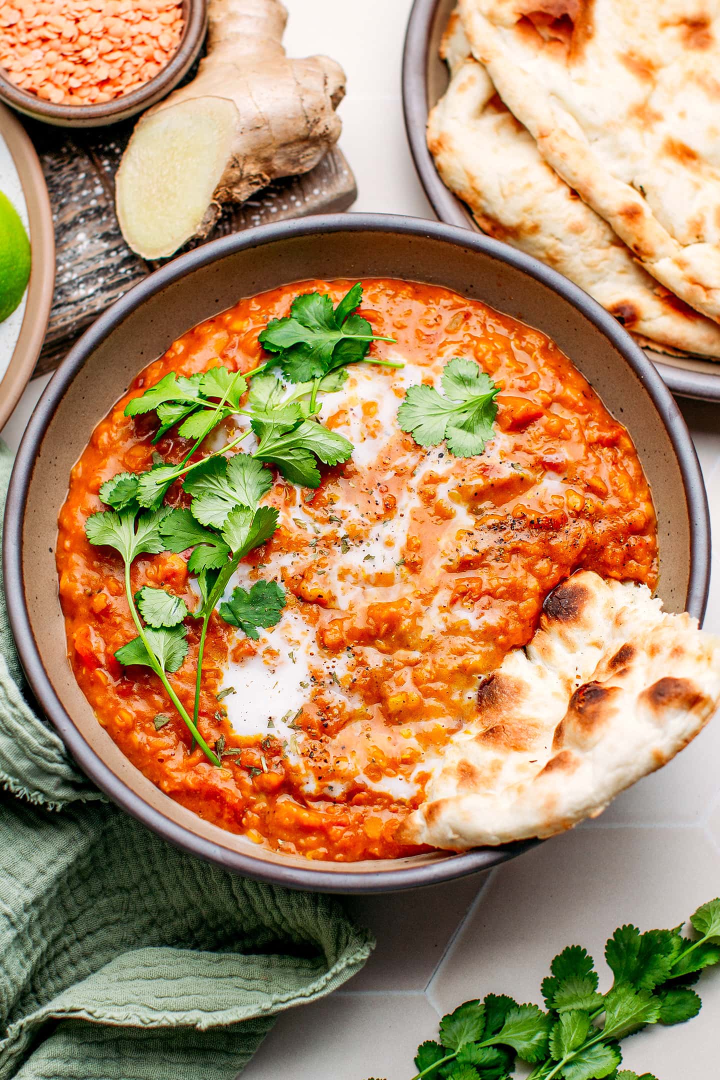 Red lentil curry in a bowl with cilantro, coconut milk, and naan.