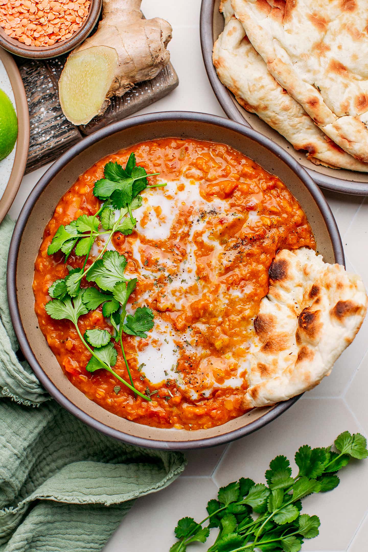 Top view of red lentil curry in a bowl with cilantro, coconut milk, and naan.