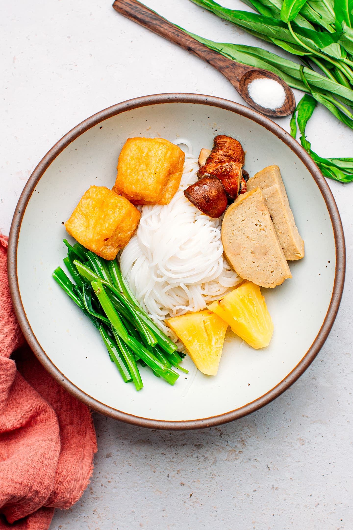 Rice noodles, pineapple, morning glory, and mushrooms in a bowl.