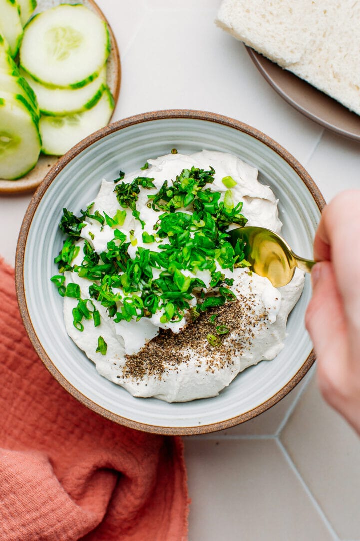 Stirring together vegan cream cheese mayo, fresh herbs, and black pepper.