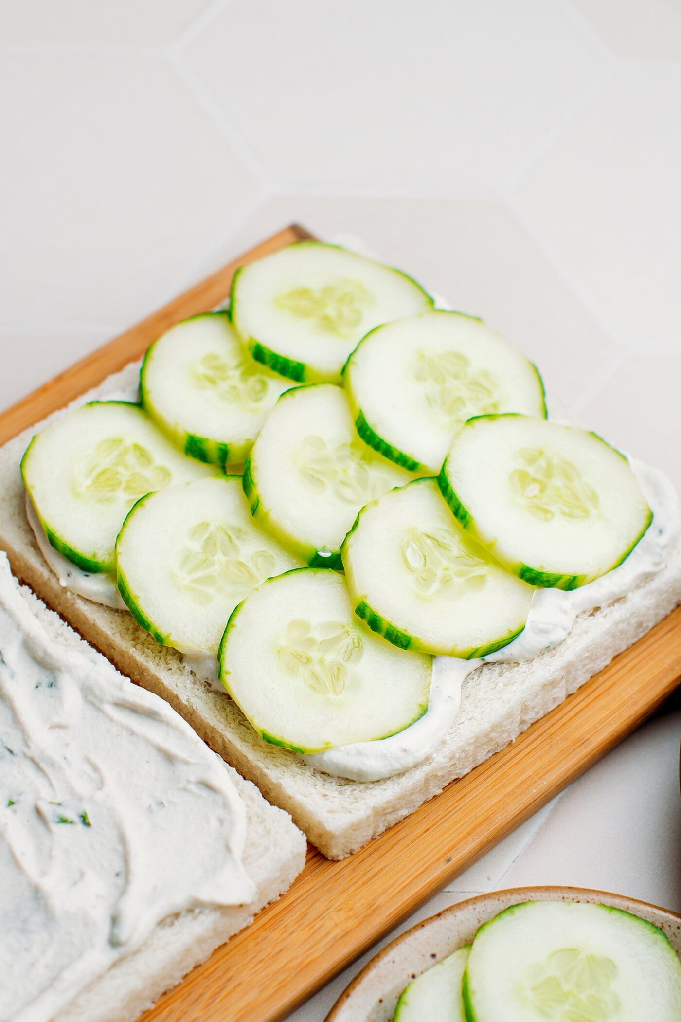 Close-up of cucumber slices with cream cheese on a slice of sandwich bread.