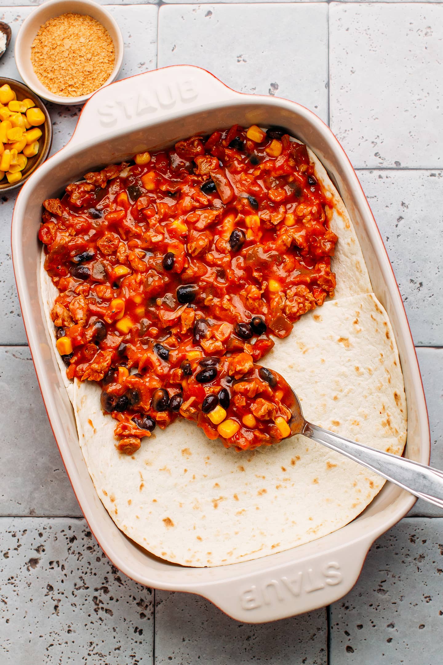 Arranging enchilada filling on top of tortillas in a baking dish.