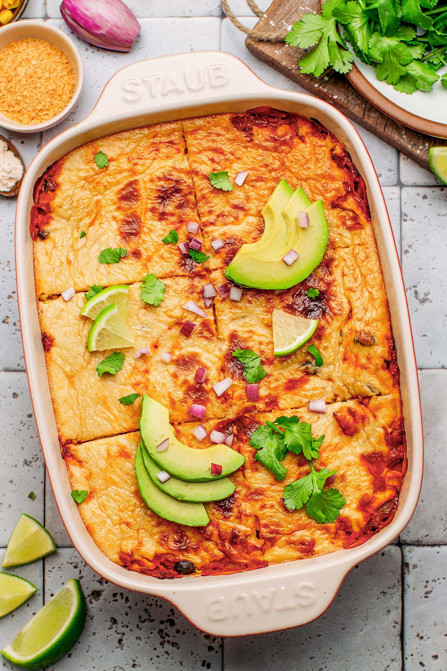 Enchilada casserole topped with lime wedges, avocado, and cilantro.