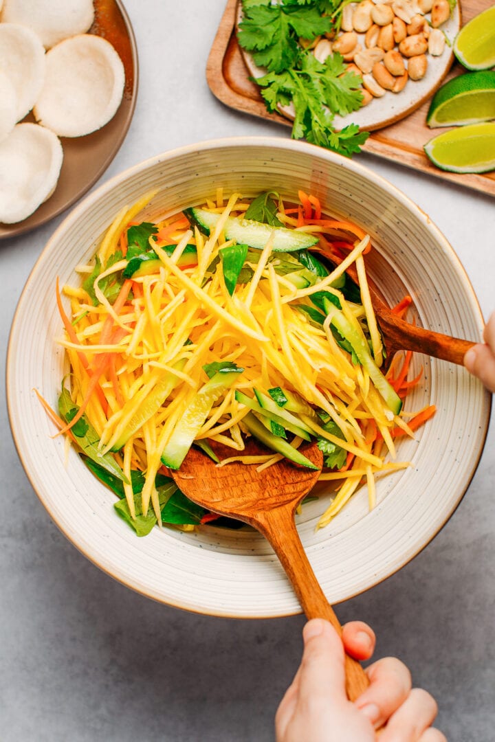 Tossing shredded mango and carrots with a dressing.
