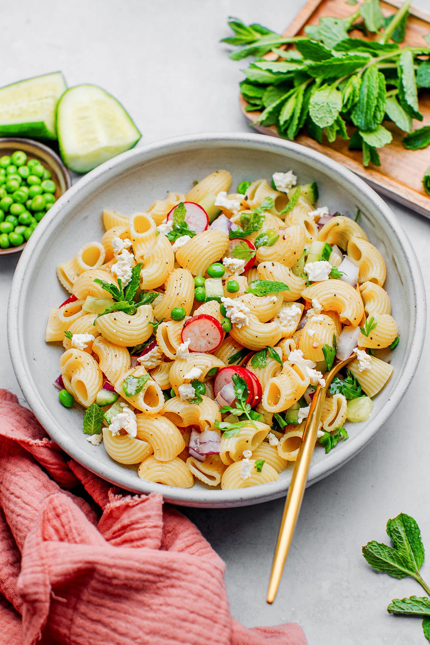 Macaroni salad with green peas, radishes, mint, and cucumber in a bowl.