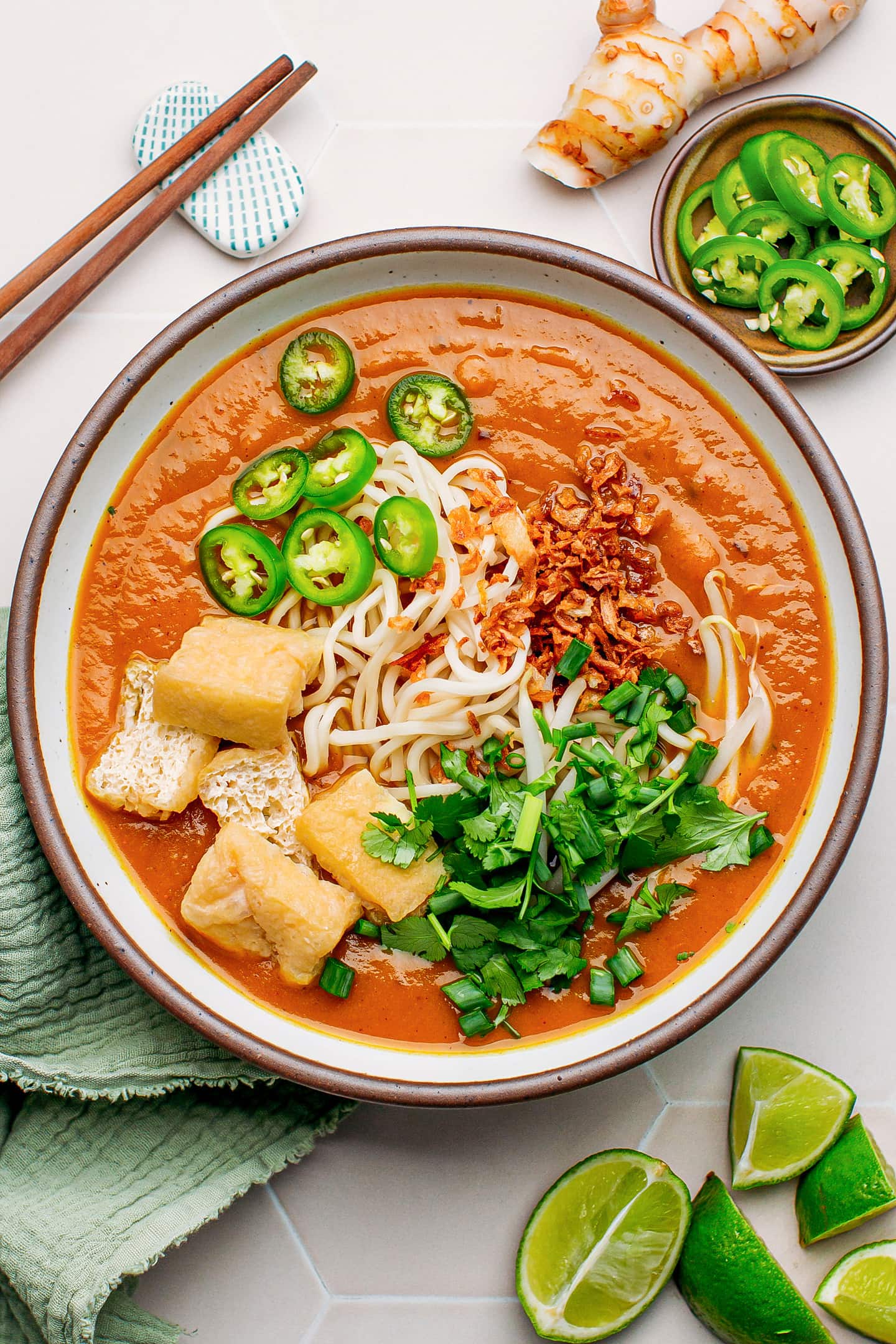 Malaysian noodle soup with green pepper slices, noodles, chopped herbs, and fried onions.