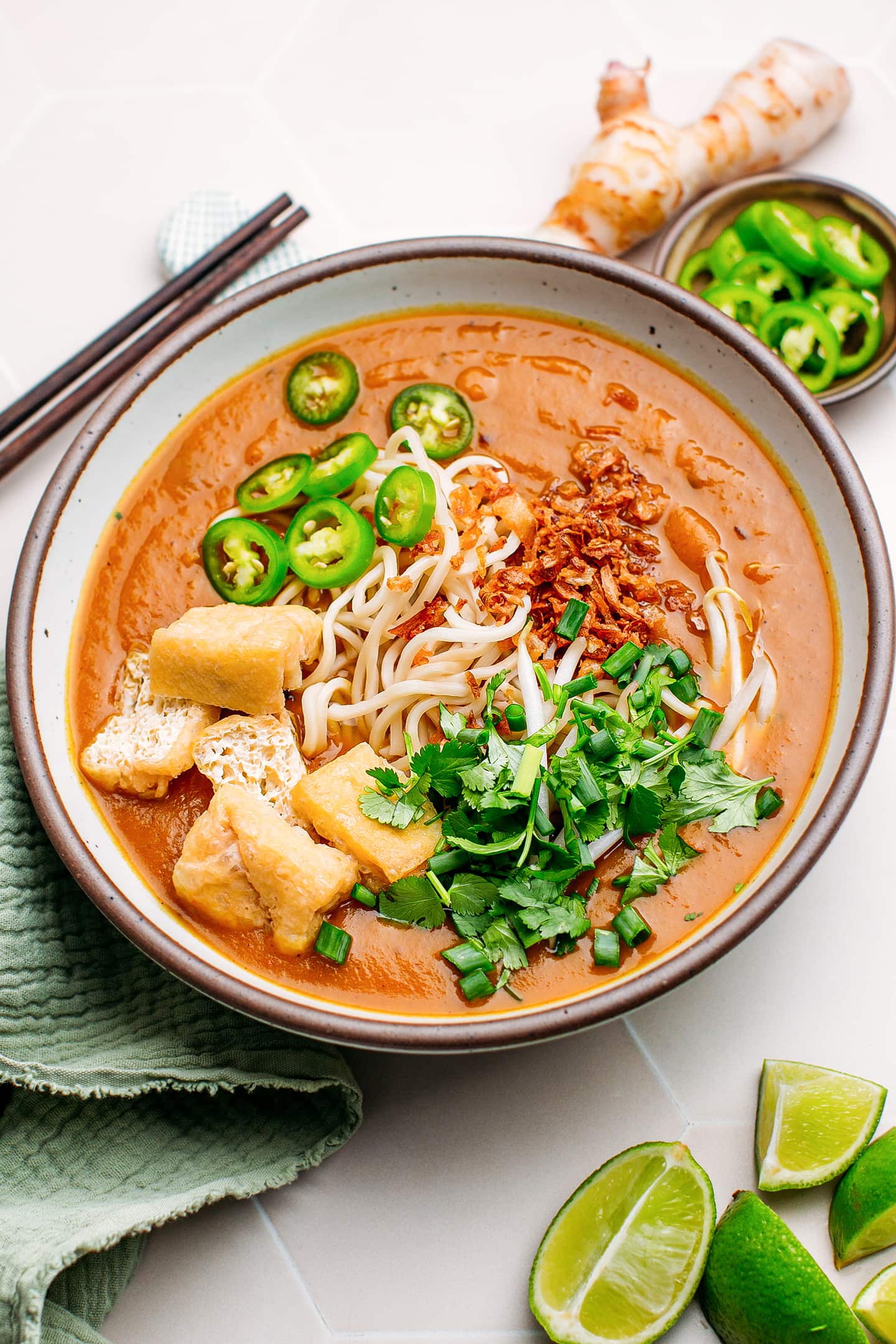 Mee rebus with green pepper slices, noodles, chopped herbs, and fried onions.