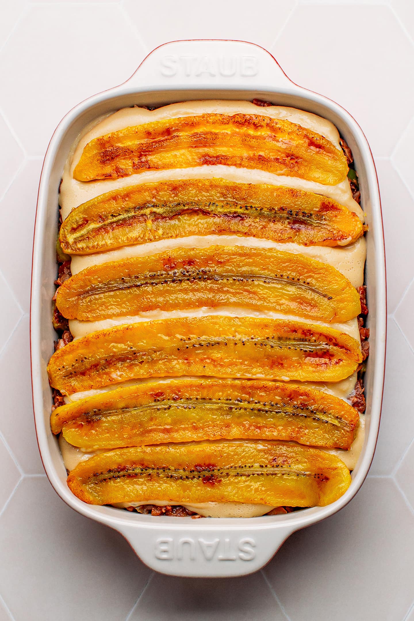 Plantains on top of vegan cheese sauce in a baking dish.