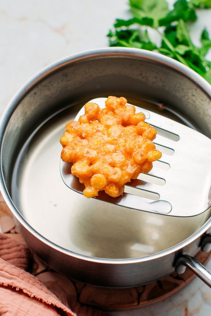 Fried corn fritters on a spatula.