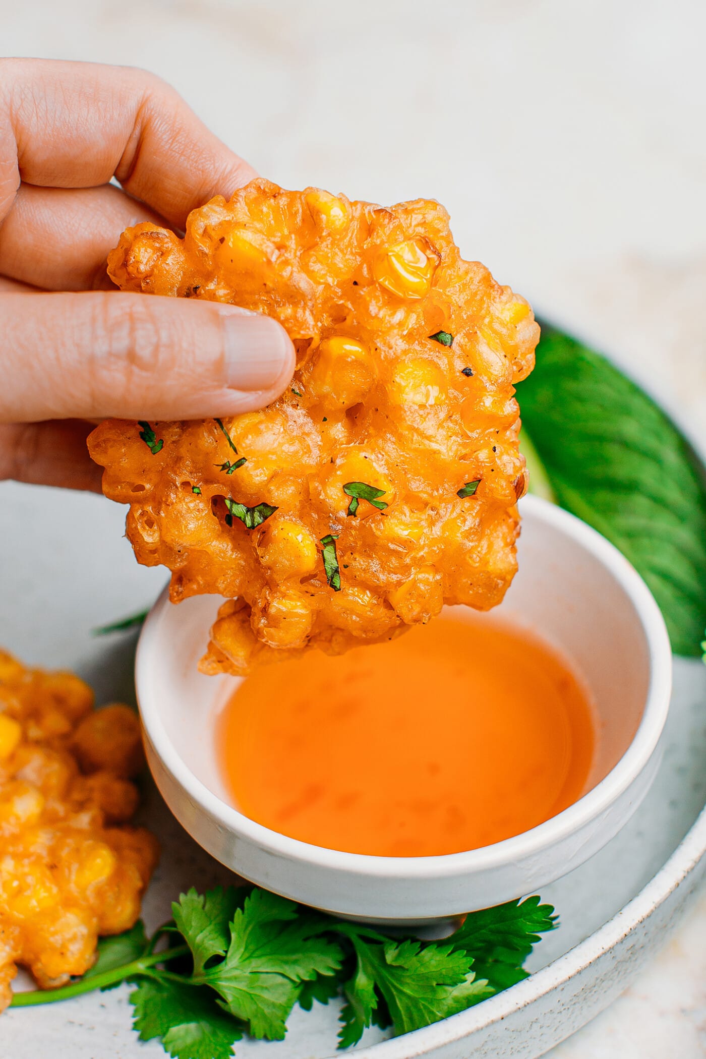 Close-up of a corn fritter over a bowl of dipping sauce.